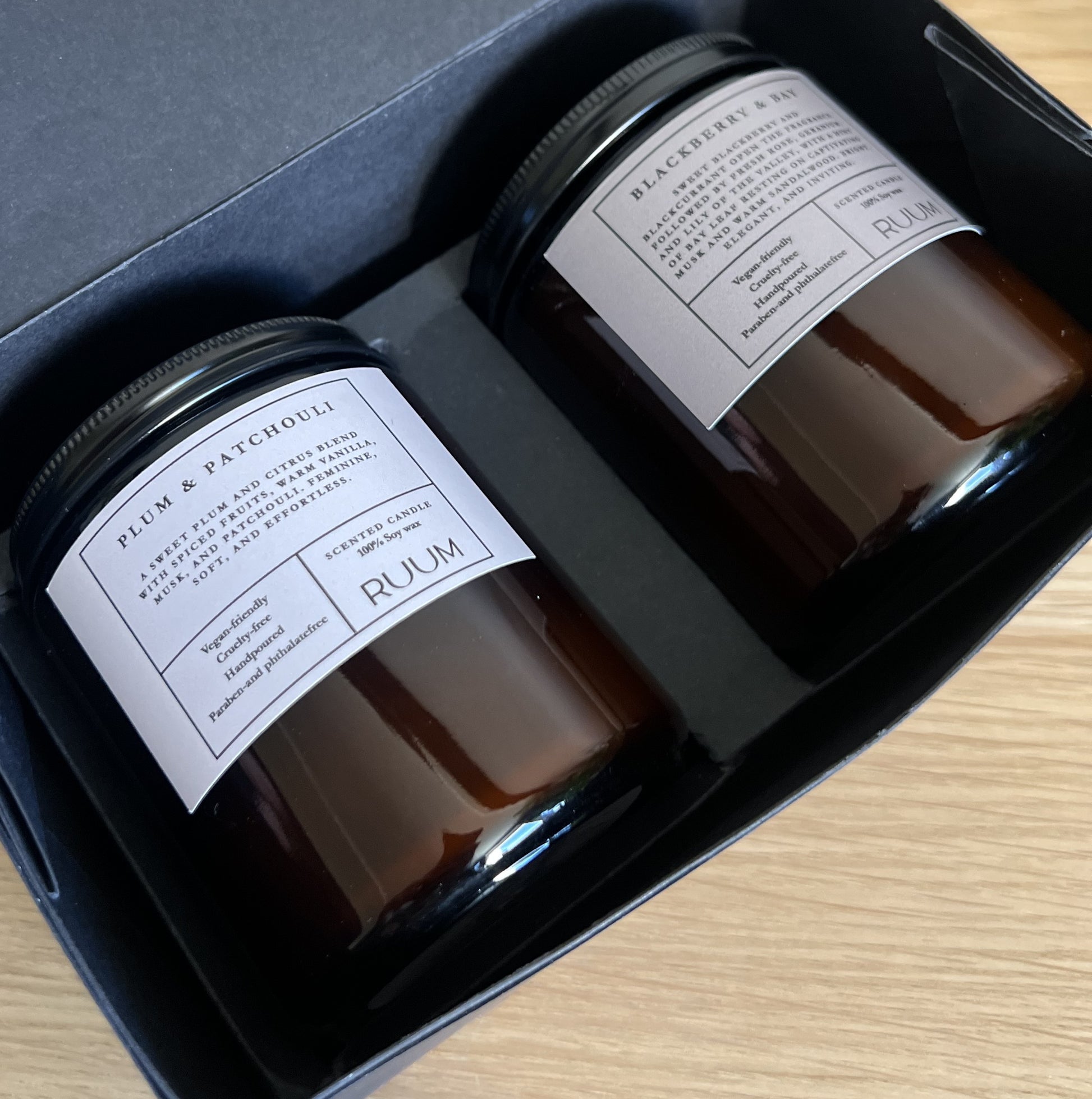 Two black jars with labels in a box on a wooden surface