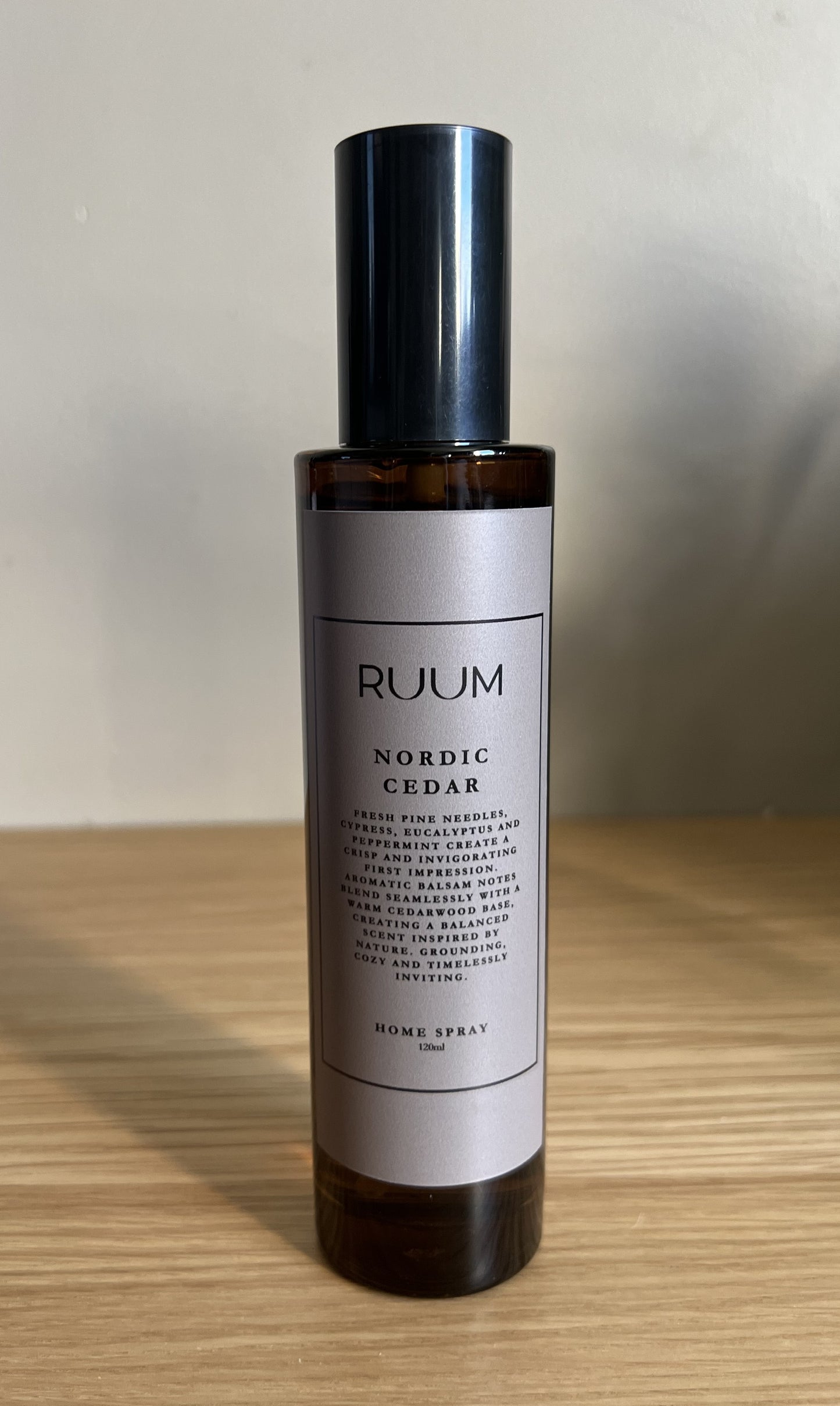 Bottle of RUUM Nordic Cedar home spray on a wooden surface with a neutral background

