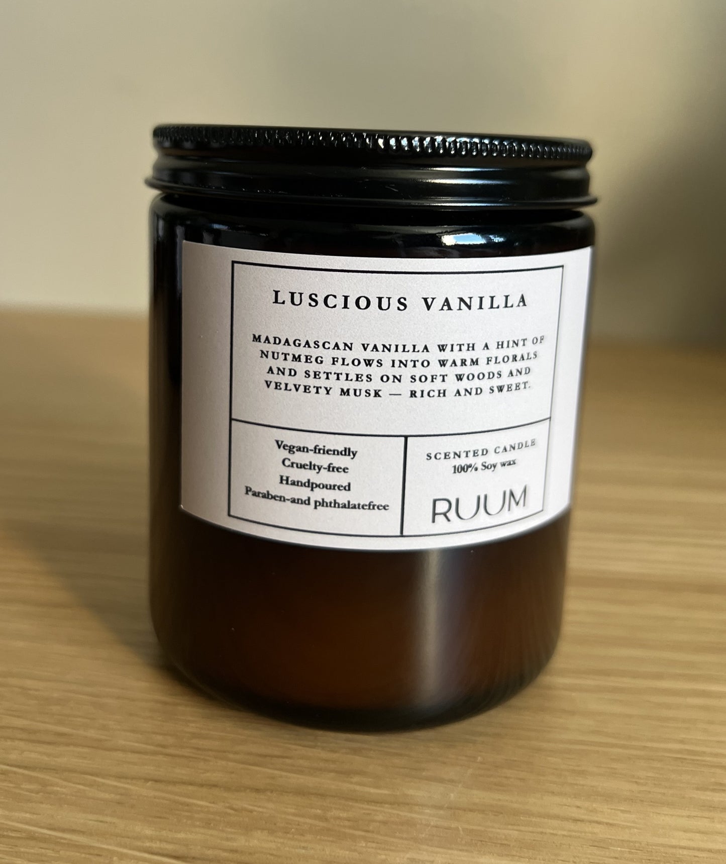 Candle jar labeled 'Luscious Vanilla' by RUUM on a wooden surface.
