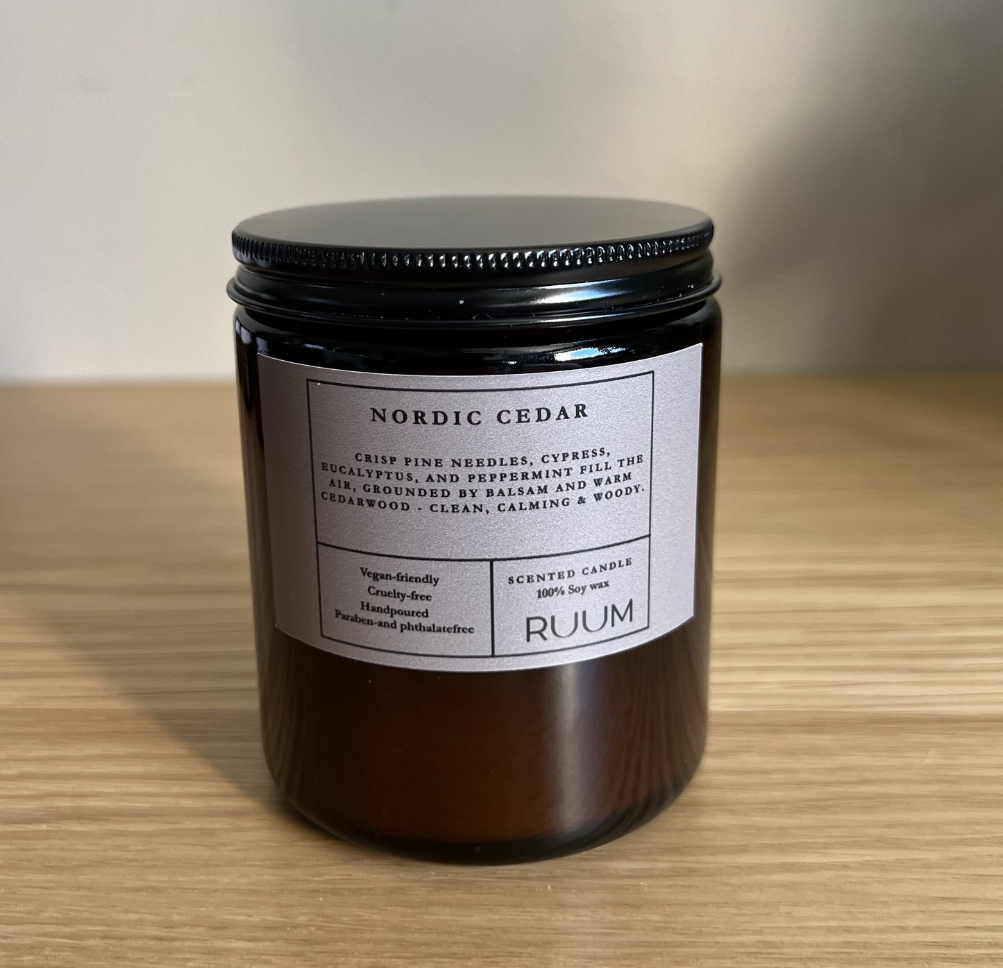 Candle jar labeled 'Nordic Cedar' by 'Ruum' on a wooden surface with a neutral background