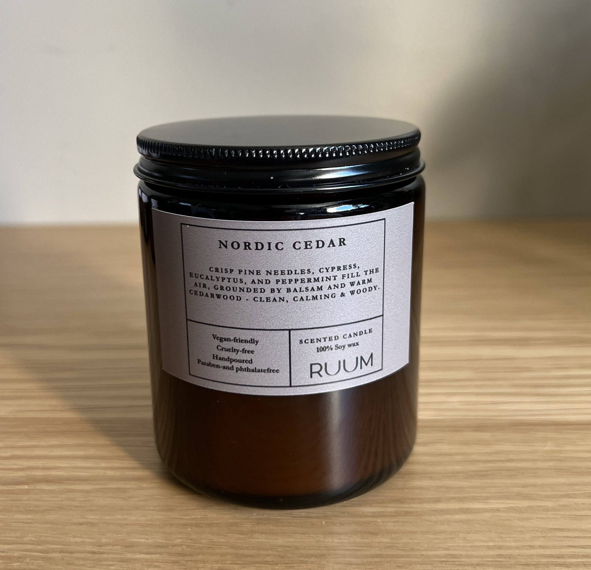 Candle jar labeled 'Nordic Cedar' by 'Ruum' on a wooden surface with a neutral background
