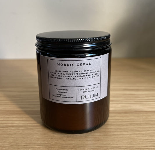 Candle jar labeled 'Nordic Cedar' by 'Ruum' on a wooden surface with a neutral background