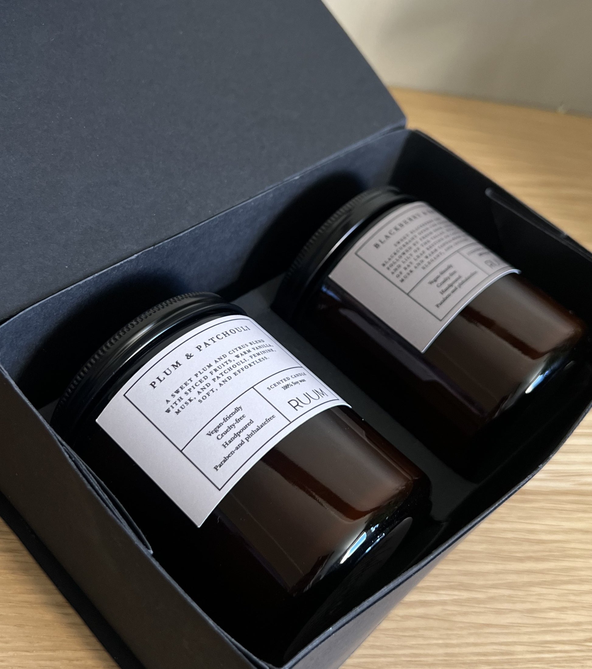 Two dark glass jars with labels in an open black box on a wooden surface.
