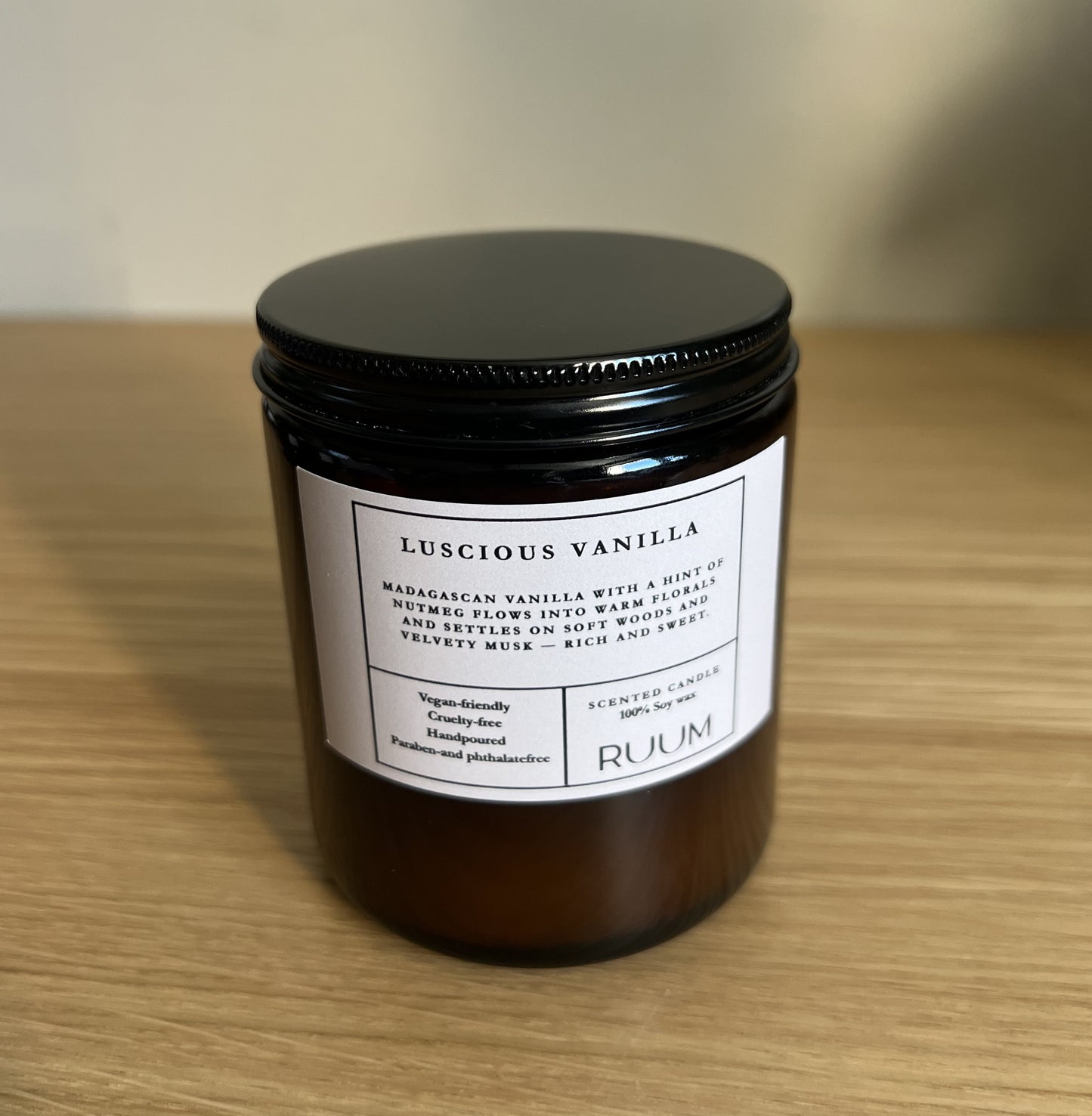 Candle jar labeled 'Luscious Vanilla' by 'Ruum' on a wooden surface.  VEgan.Crueltyfree.