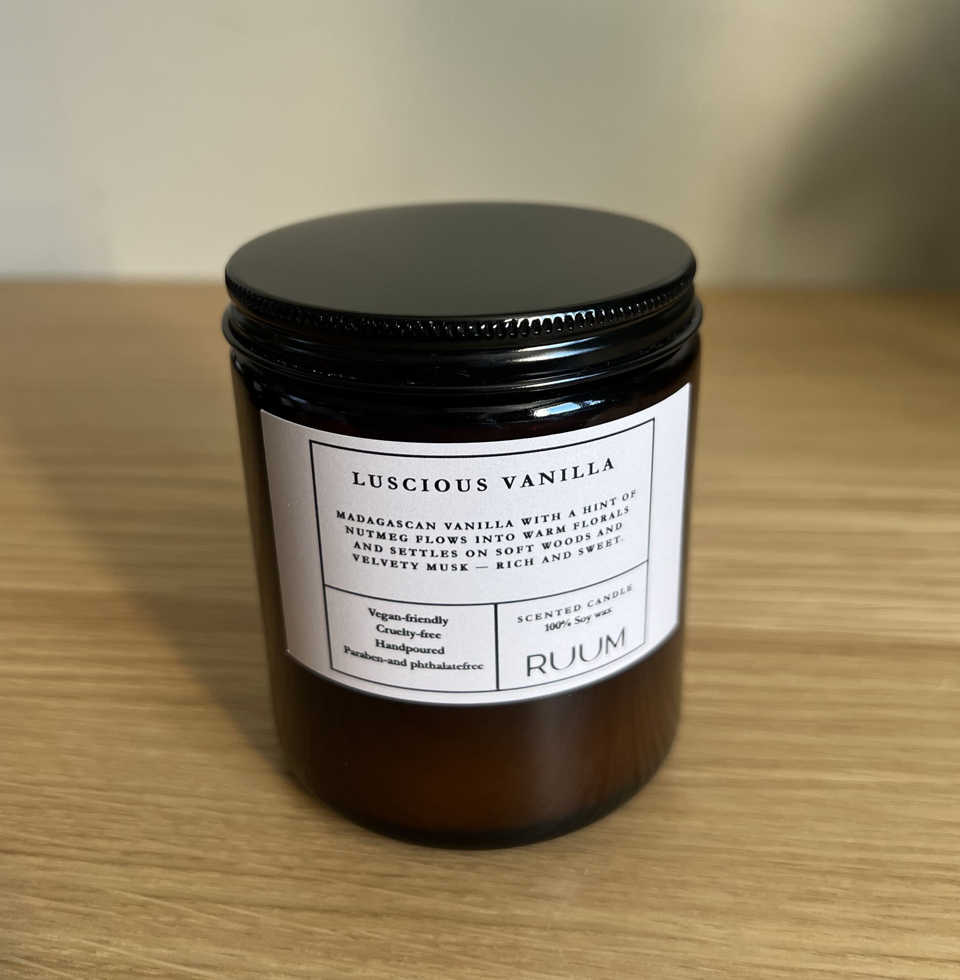Candle jar labeled 'Luscious Vanilla' by 'Ruum' on a wooden surface.  VEgan.Crueltyfree.