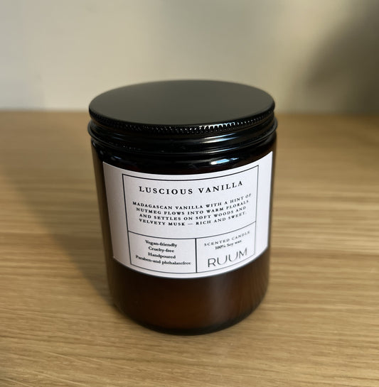 Candle jar labeled 'Luscious Vanilla' by 'Ruum' on a wooden surface.  VEgan.Crueltyfree.