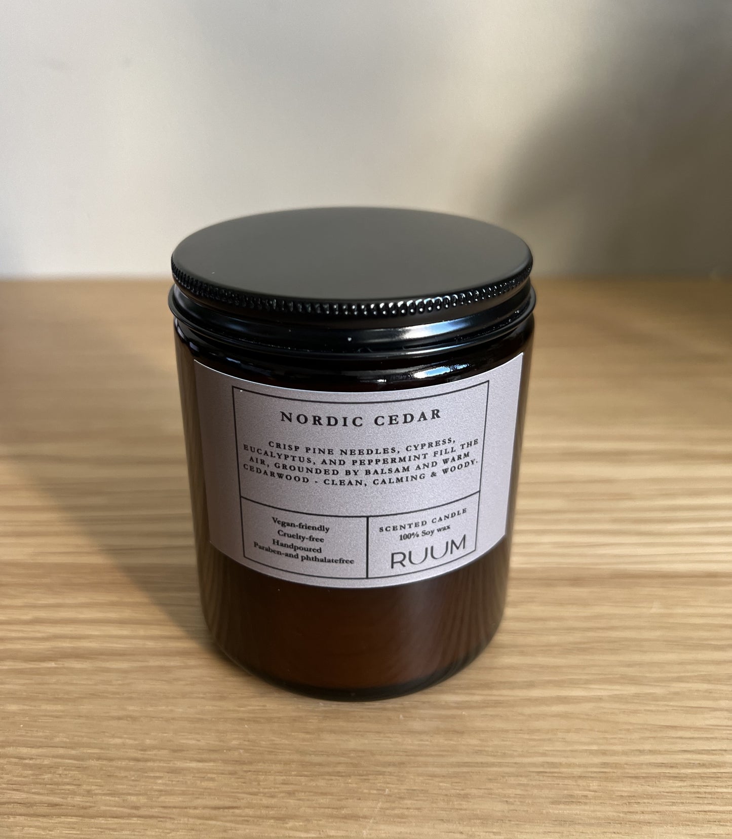 Candle jar labeled 'Nordic Cedar' by 'Ruum' on a wooden surface.

