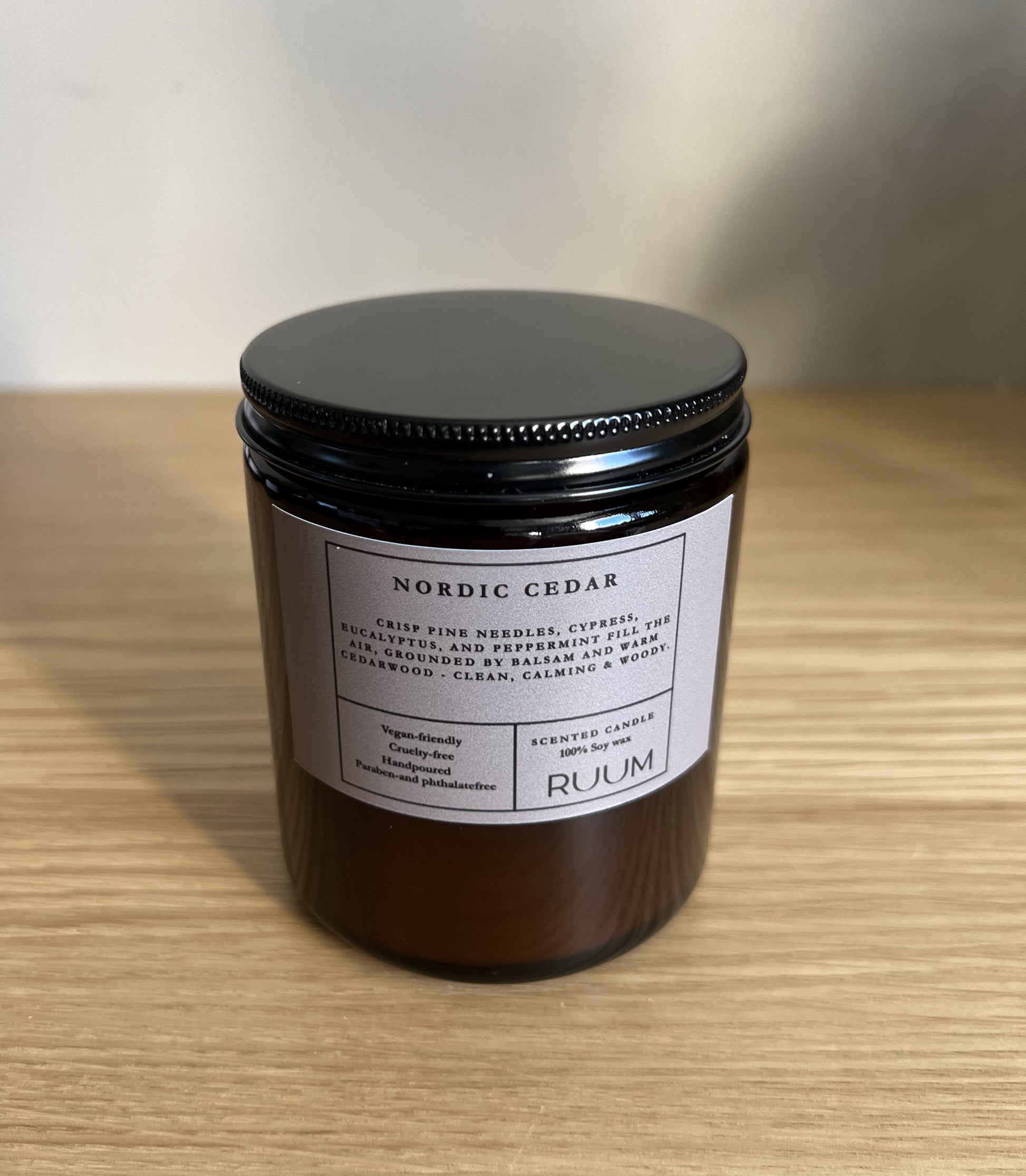 Candle jar labeled 'Nordic Cedar' by 'Ruum' on a wooden surface.

